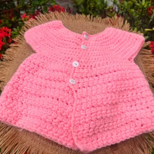 Pink crochet baby cardigan with white buttons on a woven mat