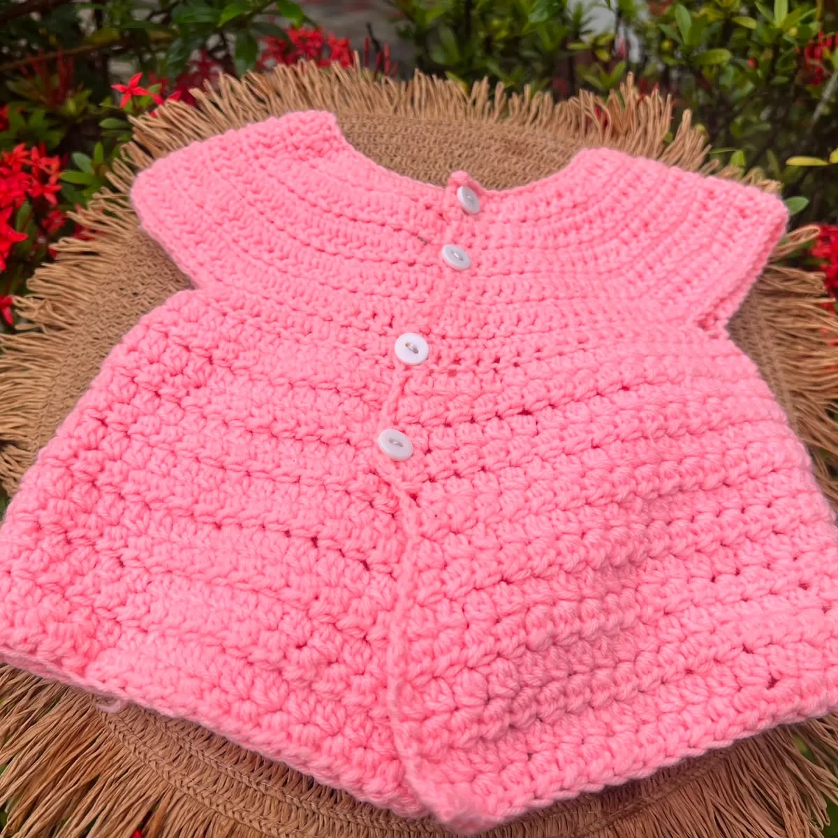 HOME Pink crochet baby cardigan with white buttons on a woven mat