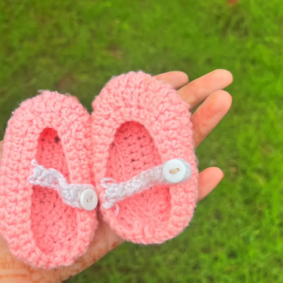 HOME Pink crochet baby booties with white button strap held in a hand