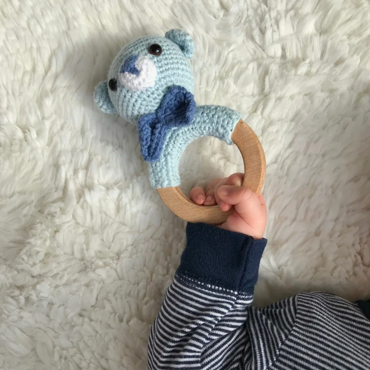 HOME Handmade crochet teddy bear rattle with wooden ring held by a baby's hand
