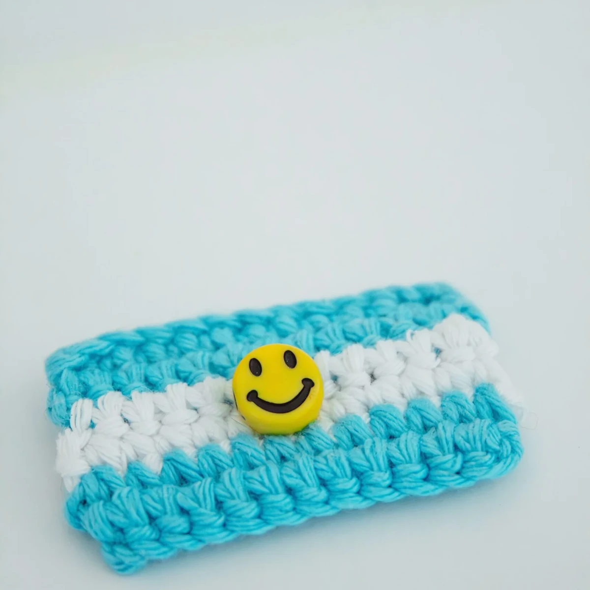 HOME Blue and white crochet pouch with a yellow smiley face charm