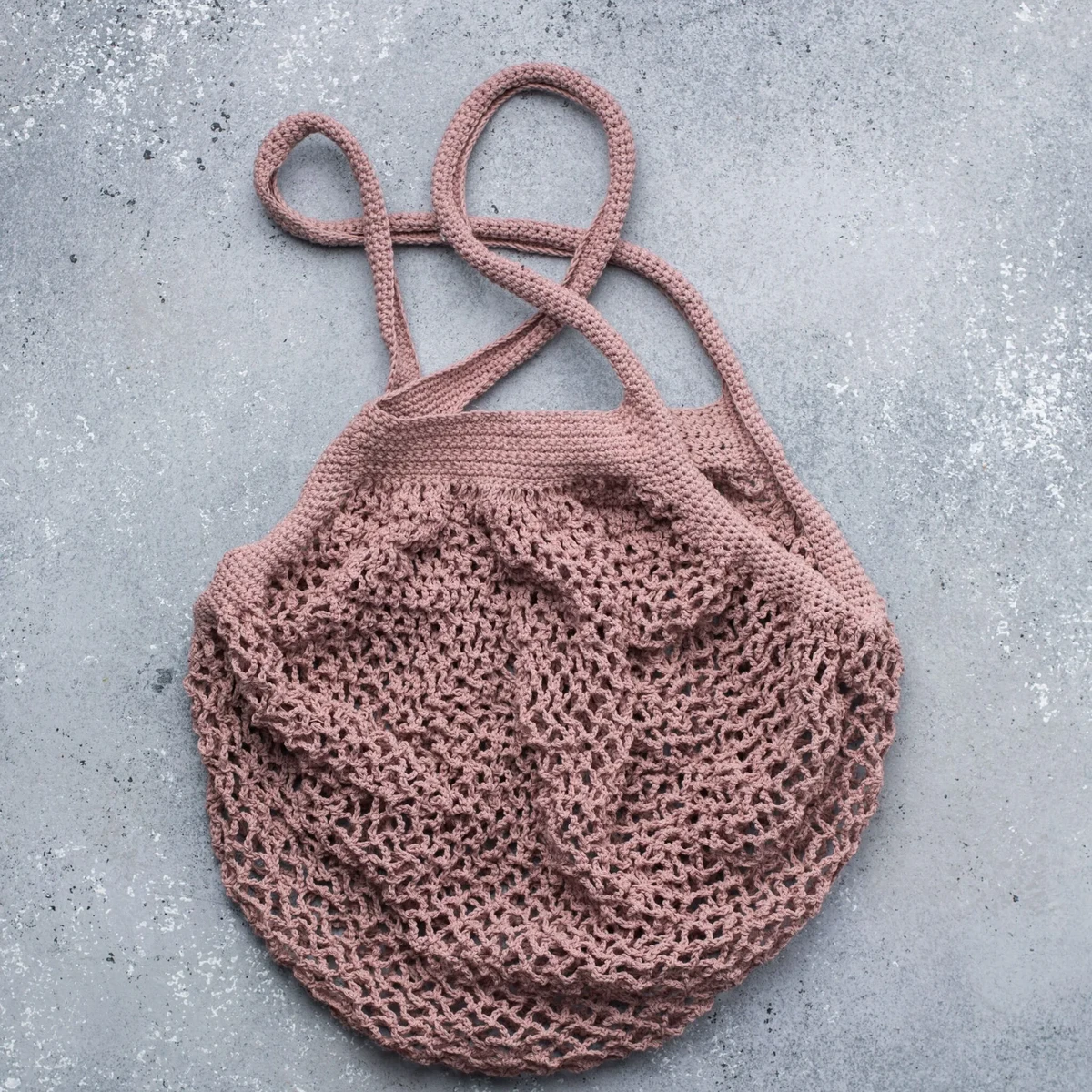 HOME Pink crochet mesh market bag on a grey stone background